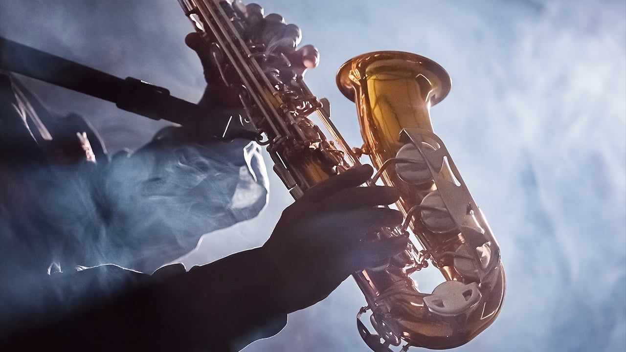 Close-up of musicians hands playing golden saxophone against blue sky with clouds