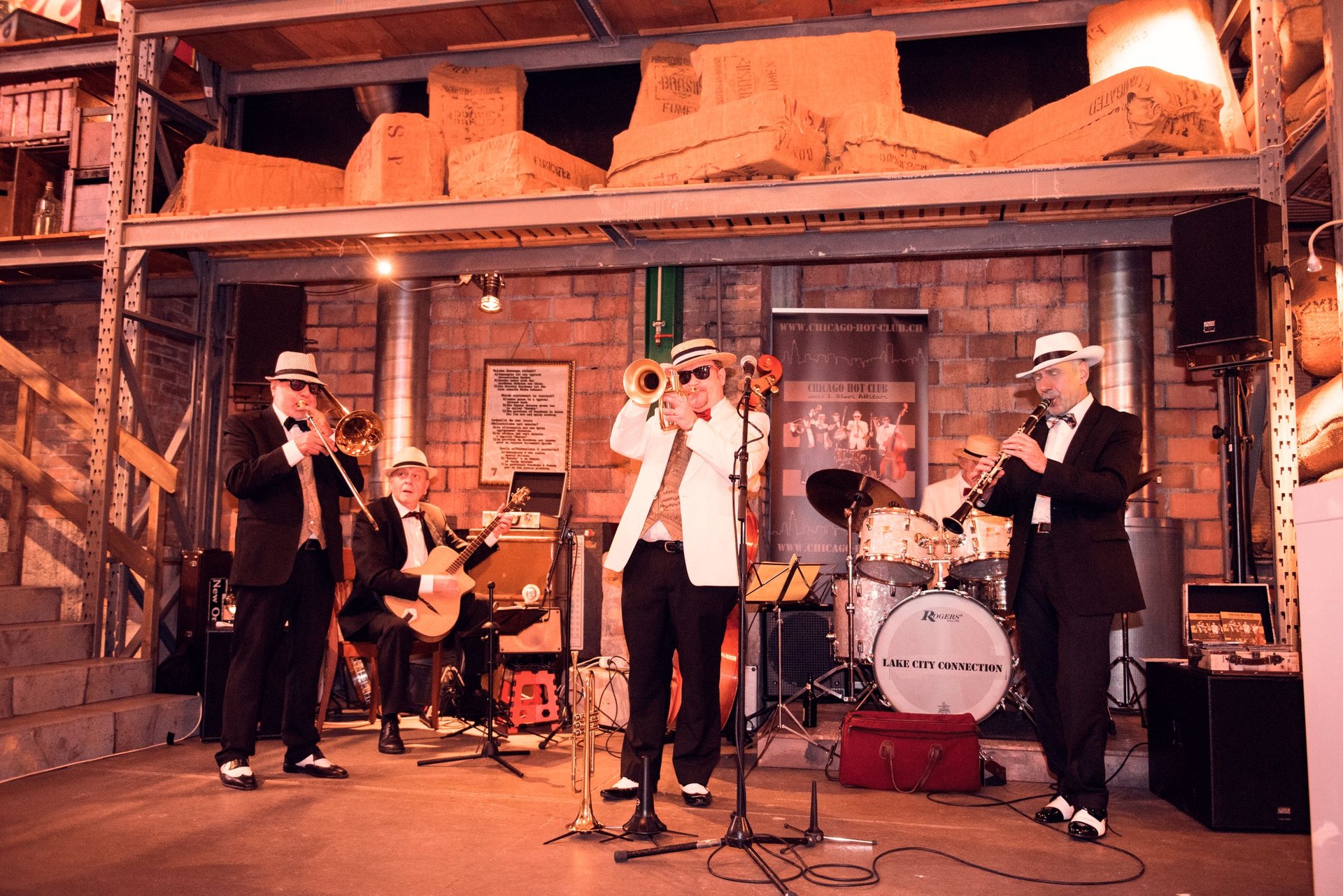 Jazz band of five musicians in suits and hats performing on stage in an outdoor venue at night