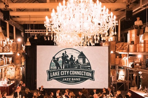 Lake City Connection Jazz Band logo displayed on a large screen in an elegant venue with ornate chandeliers and wooden interior during a live event